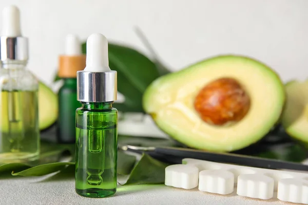 Bottles of cuticle oil, manicure instruments and avocado on light background, closeup