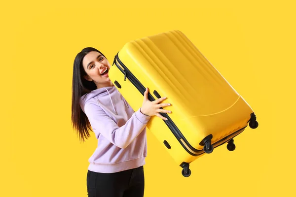 Happy young woman with suitcase on yellow background