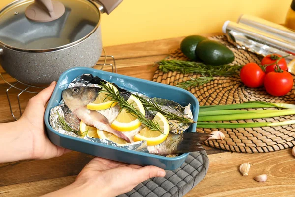 stock image Woman holding baking dish with raw fish and vegetables in kitchen