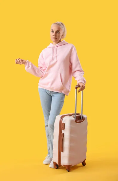 Tired mature woman with suitcase on yellow background