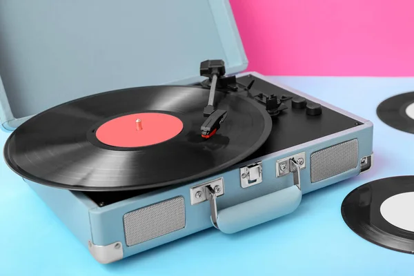 Record player with vinyl disks on table near pink wall