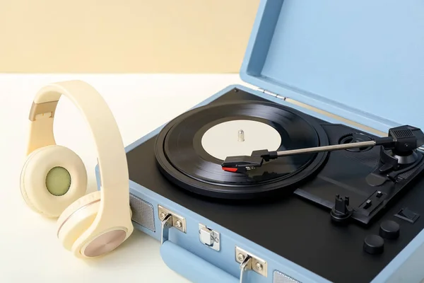 Record player with vinyl disk and headphones on table near beige wall