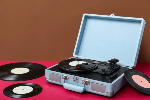 Record player with vinyl disks on table near brown wall