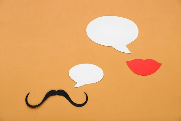 Paper mustache and lips with speech bubbles on orange background. Dialogue concept