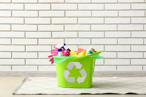 Recycling bin with cleaning supplies near white brick wall
