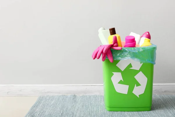 Recycling bin with cleaning supplies near light wall