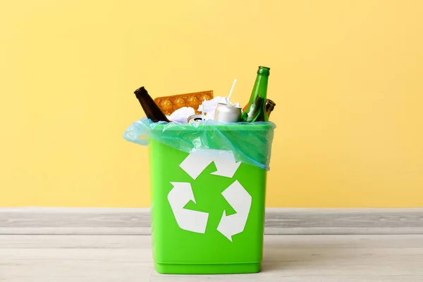 Recycling bin with garbage near yellow wall