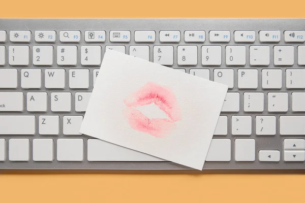 Paper with lipstick kiss mark and computer keyboard on beige background, closeup