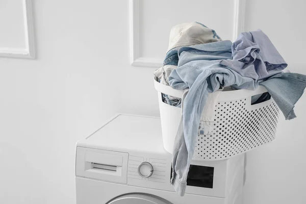 Laundry basket with dirty clothes on washing machine near light wall