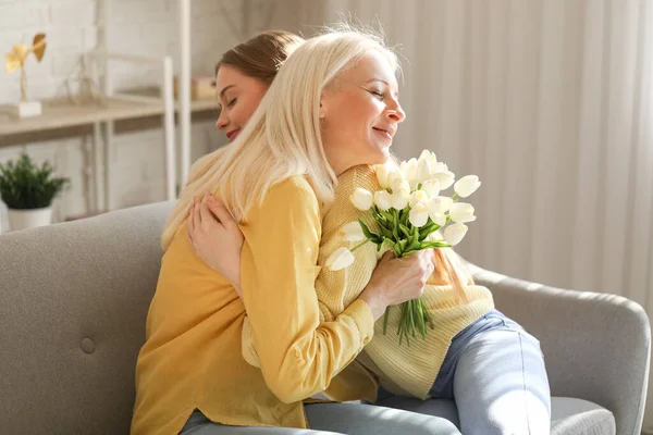 Mature woman with tulips hugging her daughter at home. Mother\'s Day celebration