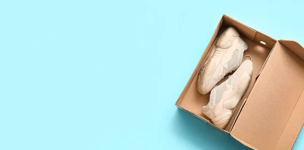 Cardboard box with sports shoes on light blue background with space for text