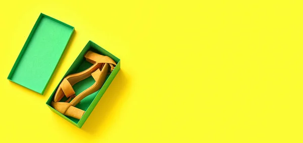 Cardboard box with high heeled sandals on yellow background with space for text