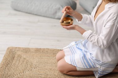 Beautiful young woman with Tibetan singing bowl at home