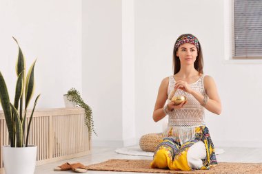 Young woman with Tibetan singing bowl sitting on mat at home