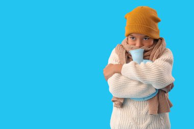 Mavi arka planda sıcak su şişesi olan donmuş Afro-Amerikalı çocuk.