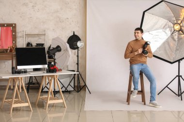 Profesyonel kameralı genç bir erkek fotoğrafçı stüdyoda oturuyor.