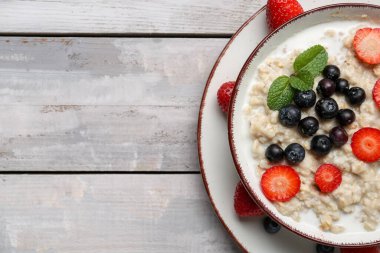Ahşap arka planda lezzetli yulaf ezmesi, yabanmersini ve çilekli kase.