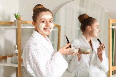 Zerdeçal maskeli ve banyoda fırça kullanan genç bir kadın.