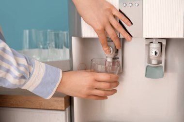 Kadın modern soğutucudan bardağa su döküyor.