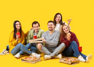 Sarı arka planda lezzetli pizza ve içecekler olan bir grup arkadaş.