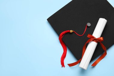 Kırmızı kurdeleli diploma ve mavi arka planda mezuniyet şapkası