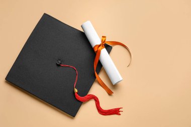 Kırmızı kurdeleli diploma ve bej arka planda mezuniyet şapkası.