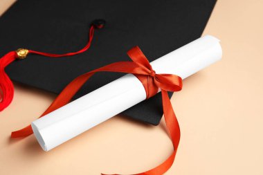 Kırmızı kurdeleli diploma ve bej arka planda mezuniyet şapkası.