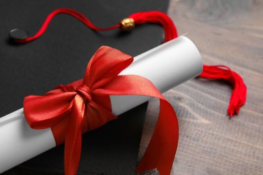 Diploması kırmızı kurdele ve ahşap masada mezuniyet şapkası.