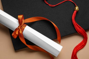 Kırmızı kurdeleli diploma ve bej masadaki mezuniyet şapkası.