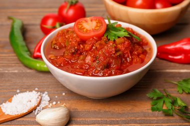 Bir kase lezzetli salsa sosu ve kahverengi ahşap masadaki malzemeler.