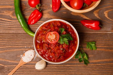 Bir kase lezzetli salsa sosu ve kahverengi ahşap masadaki malzemeler.