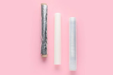 Alüminyum folyo ruloları, fırın kağıdı ve pembe arka planda yemek filmi.