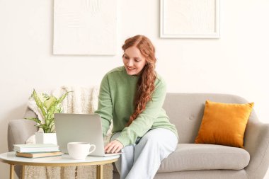 Evde dizüstü bilgisayar kullanan güzel kızıl kadın.