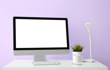 Leylak duvarının yanında bilgisayar, bardak ve lamba olan işyeri