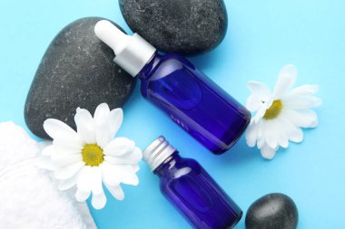 Renkli arkaplanda manikür yağı şişeleri, spa taşları ve papatya çiçekleri olan kompozisyon, yakın plan