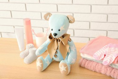 Bebek kıyafetleri ve aksesuarları olan oyuncak ayı beyaz tuğla duvarın yanındaki masada.