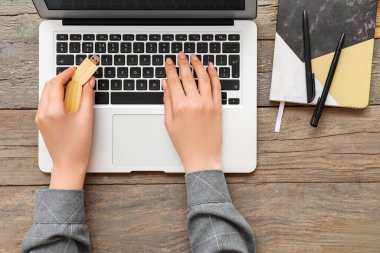 Modern dizüstü bilgisayarı, USB belleği, not defteri ve tahta arka planda kalemleri olan kadın eller.