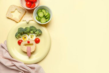 Bej arka planda yüz ve sebze şeklinde komik bir kahvaltı tabağı.