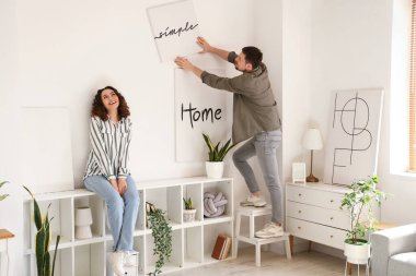 Genç bir çift evdeki ışık duvarına poster asıyor.