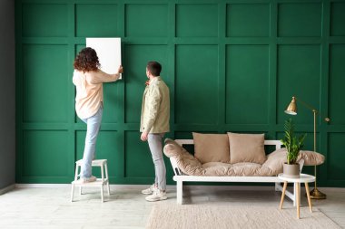 Evdeki yeşil duvara boş posterler asan genç çift.