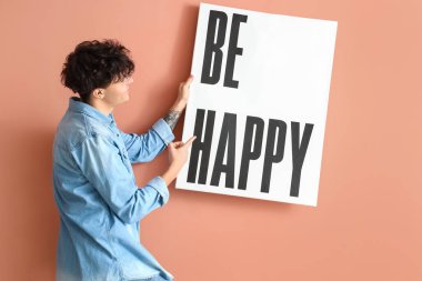 Genç adam pembe duvara poster asıyor.