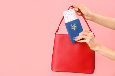 Kadın Ukrayna pasaportunu pembe arka planda çantaya koyuyor.