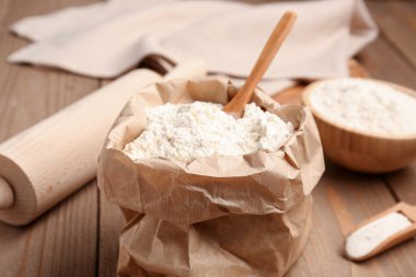 Tahta masa üzerinde buğday unu ve kepçe kağıt torba, yakın plan.