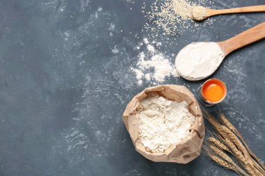 Kağıt torba un, kırık yumurta, kaşık ve buğday kulakları gri grunge masasında.