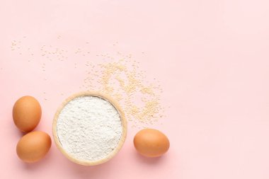 Pembe arka planda buğday unu, susam tohumu ve yumurtalı kase.
