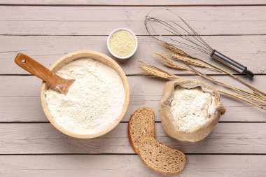 Buğday unu, ekmek, susam tohumu ve gri ahşap masada çırpma kabı.