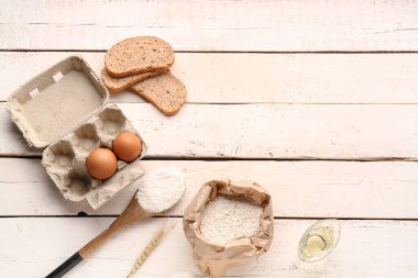 Buğday unu, yumurta, ekmek parçaları ve beyaz ahşap masa üzerinde kaşık içeren kompozisyon
