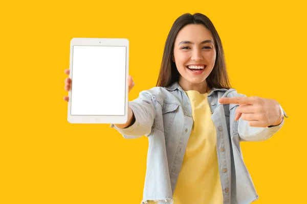 Young woman pointing at big tablet computer on yellow background