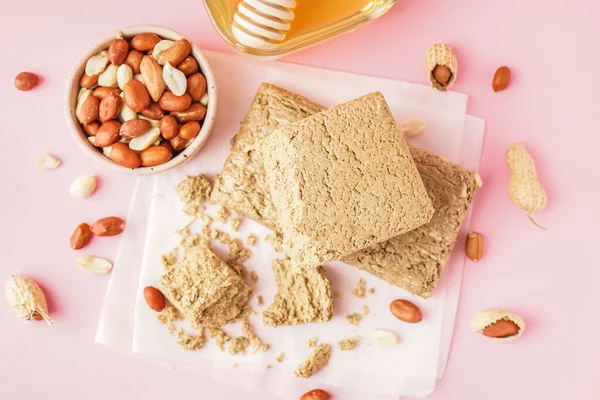 stock image Tasty halva and bowl of peanuts on pink background