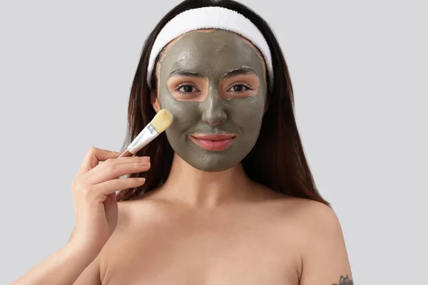 Cosmetologista Aplicando Máscara Barro Rosto Jovem Fundo Cinza Close — Fotografia de Stock
